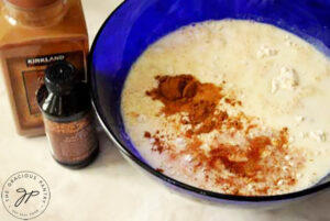 Cinnamon and vanilla extract added to waffle batter in a blue mixing bowl.