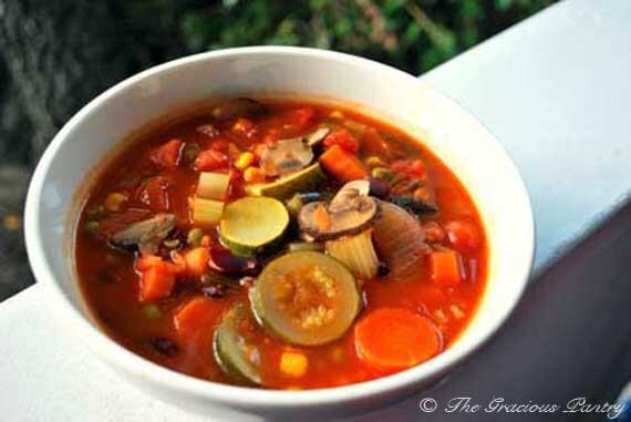 Vegan Minestrone Soup in a white bowl sitting outside on a white railing. The soup is filled with tons of veggies and has a deep orange-red color.