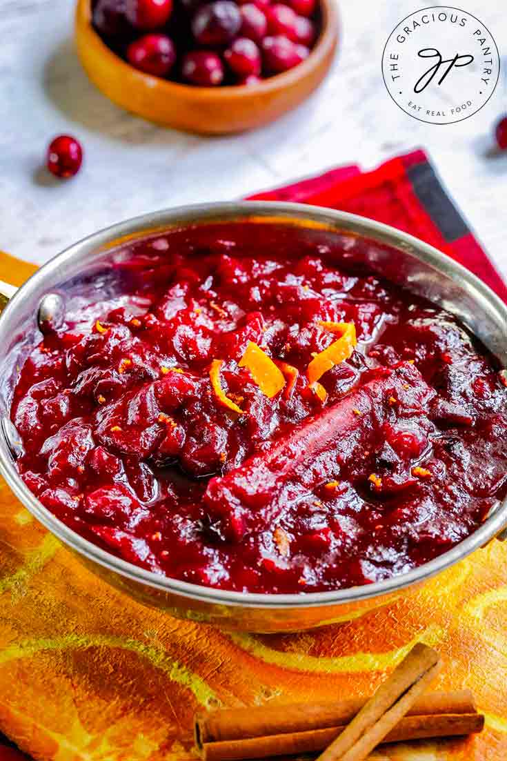 A bowl of this Homemade Cranberry Sauce sits on an orange cloth. It is garnished with orange peel.