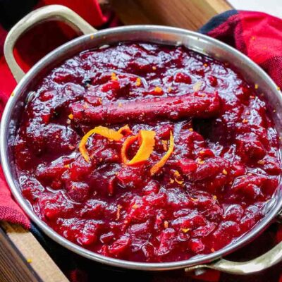 This Homemade Cranberry Sauce is being served in a bowl. Looking from the top down, you can see all the cooked, bright red cranberries, the cinnamon stick and the orange peel garnish. It's ready to eat!