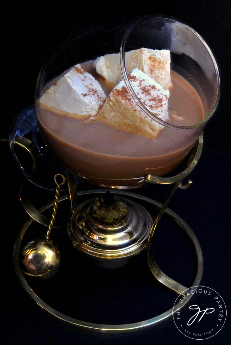 A brandy warmer sits filled with hot chocolate and three square marshmallows.
