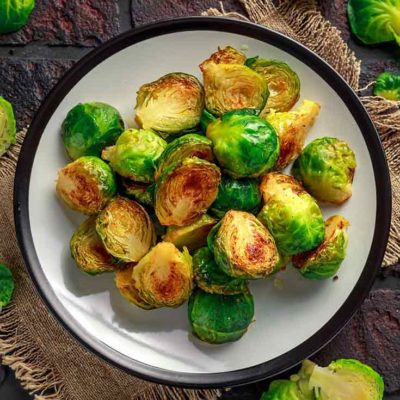 A single plate sits on a dark, brick background. It holds a beautiful pile of roasted, golden-brown brussels sprouts which have been cut in half.
