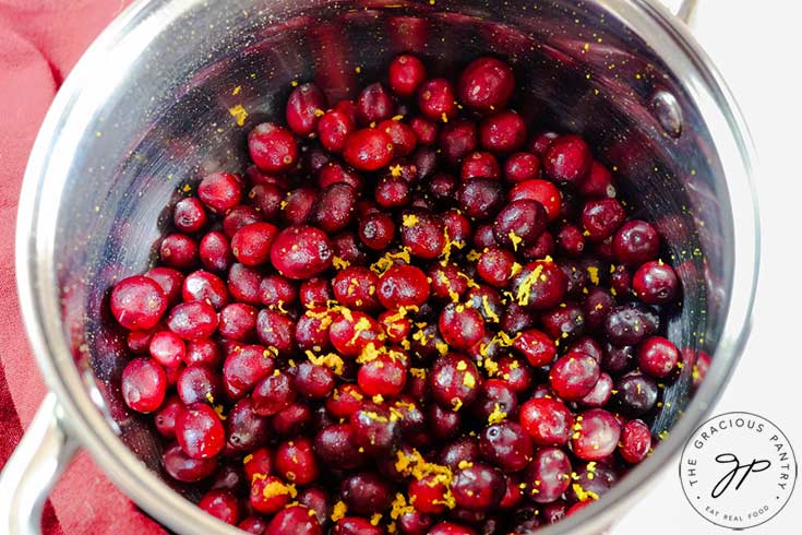 Fresh cranberries in a pot with orange zest sprinkled on top.
