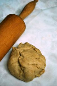 A ball of pie dough with a rolling pin laying next to it.