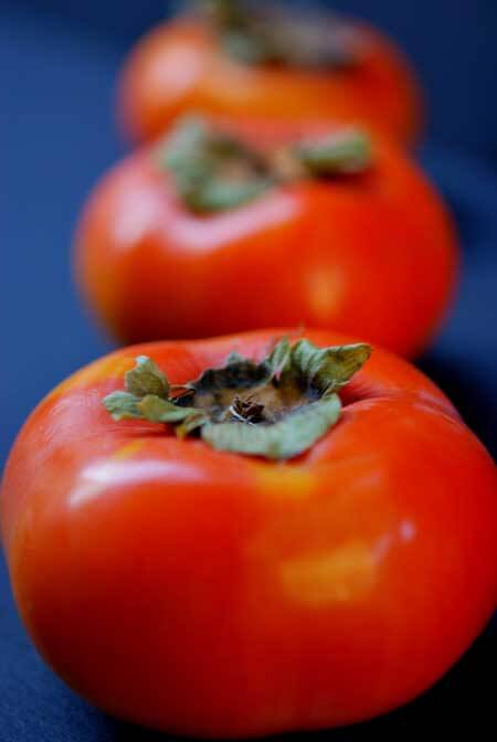 Three Fuyu Persimmons in a row on a dark background.