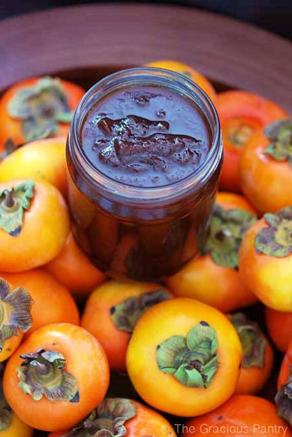 Clean Eating Persimmon Jam displayed in an open jar amidst a bed of fresh persimmons.