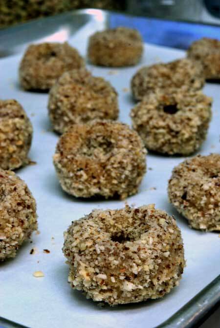 Healthy thumbprint cookies lined up on a parchment-lined cookie sheet that are not yet filled with jam.