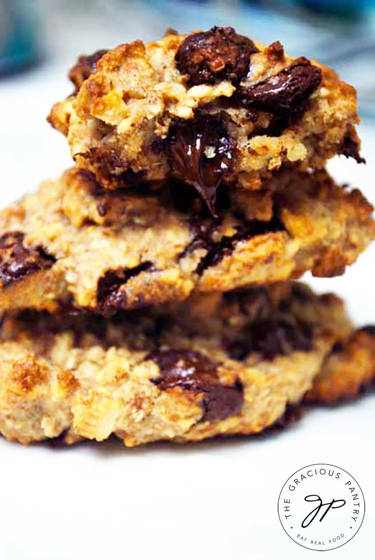 A stack of 3 Clean Eating Chocolate Chip Cookies with a bite taken out of the one on top. The warm chocolate chip that was bitten is oozing down out of the cookie.