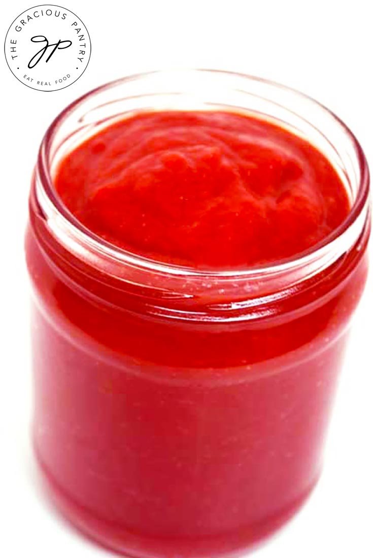 An open jar of this bright red, Homemade Ketchup Recipe sits on a white background.