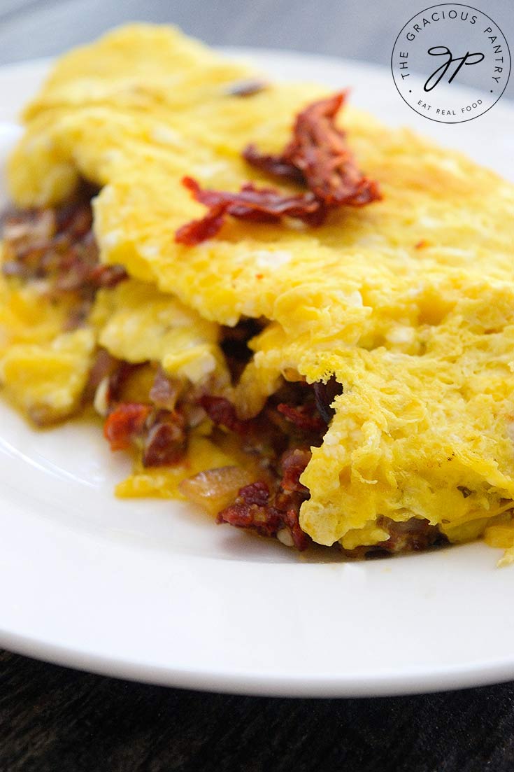 A delicious, Sun Dried Tomato Omelet sits served on a white plate, ready to eat.