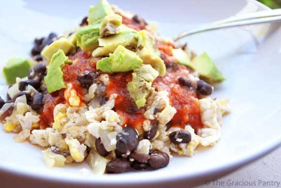A white bowl of Clean Eating Black Bean Scramble. You can see the layers of ingredients with eggs on the bottom, then the beans, salsa and finally the avocado on top.