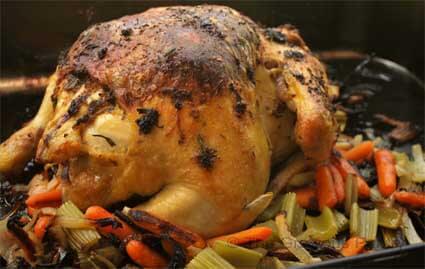 A Whole Roasted Chicken in a roasting pan with vegetables.