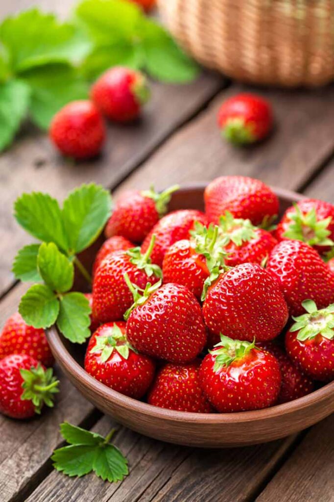 Whole strawberries in a wooden bowl on a wooden table.