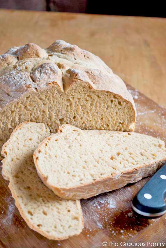 A loaf of Irish soda bread sits on a cutting board with two slices cut and laying on the cutting board in front of it.