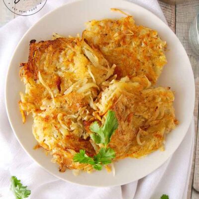 This Homemade Hash Browns Recipe has been served on a white platter. A big stack of golden brown hash browns sits on a white plate, ready to eat.