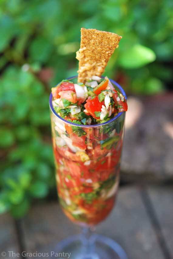 Clean Eating Cilantro Salsa piled high in a clear champaign glass with a corn chip on top for garnish.