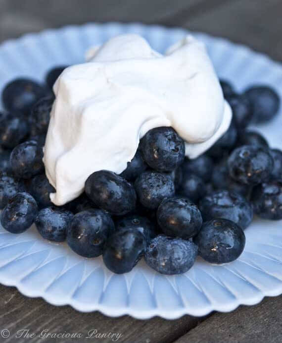 Clean Eating Coconut Whipped Cream A plate of fresh blueberries is shown up close with this Clean Eating Coconut Whipped Cream laying over the top of them.