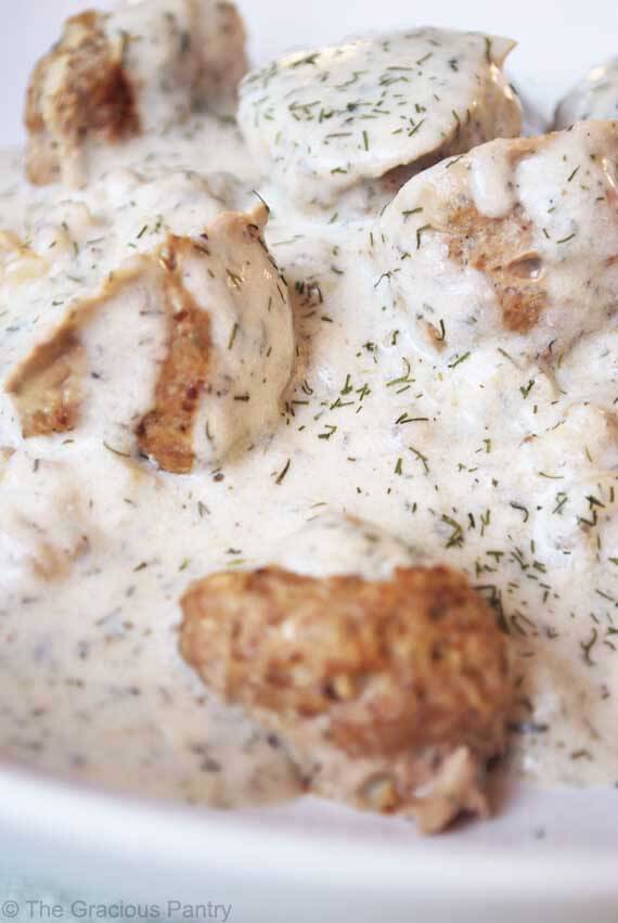 A close up shot of these Clean Eating Danish Meatballs covers in white sauce. You can see flecks of dill throughout the sauce.