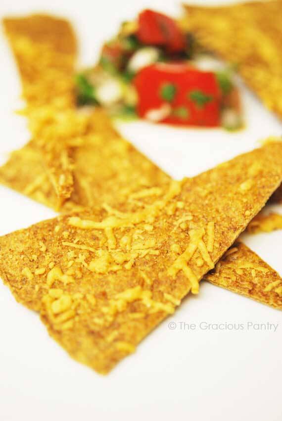 A few Clean Eating Wheat Tortilla Chips are shown up close and scattered on a white surface.