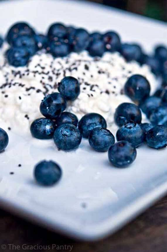 A close up shot of this Clean Eating Blueberry Cottage Cheese shows a square, white plate holding a layer of cottage cheese with blueberries and chia seeds sprinkled over the top.