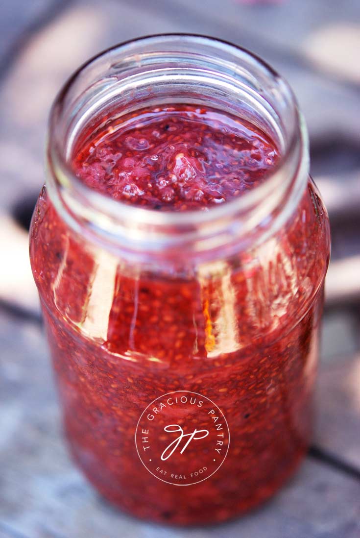 Clean Eating Strawberry Chia Seed Spread Recipe shown in a clear glass jar filled nearly to the top with the bright red strawberry spread.