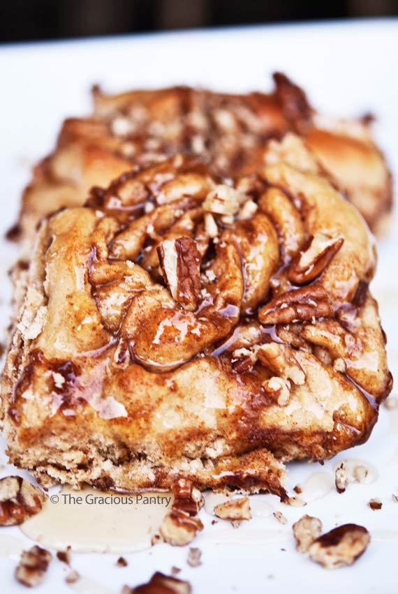 Clean Eating Cinnamon Rolls shown up close on a white platter. You can see the glaze of honey over the buns and pieces of pecans are sprinkled over the top.