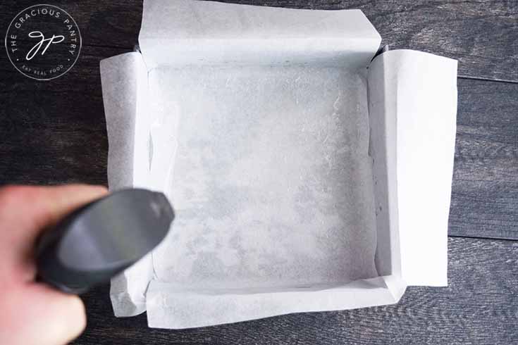 Spraying a parchment lined brownie pan with an oil sprayer.