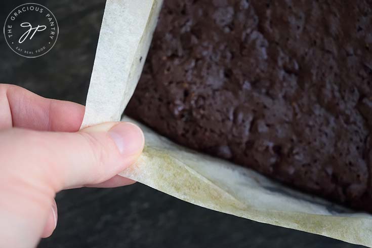 Using the parchment paper to lift the brownies out of the baking pan.