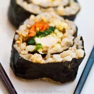 Chicken Sushi lined up on a white plate with black chopsticks.