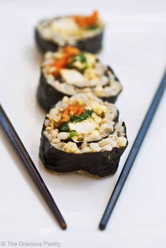 Chicken sushi slices lined up in a row next to chop sticks.