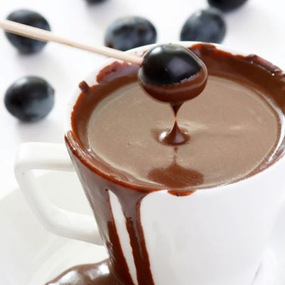 A single blueberry on a toothpick being dipped into a white bowl filled with Clean Eating Chocolate Fondue Recipe