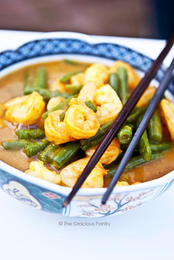 Clean Eating Coconut Curry Shrimp sits in a bowl with the green beans and shrimp stacked high in the broth.