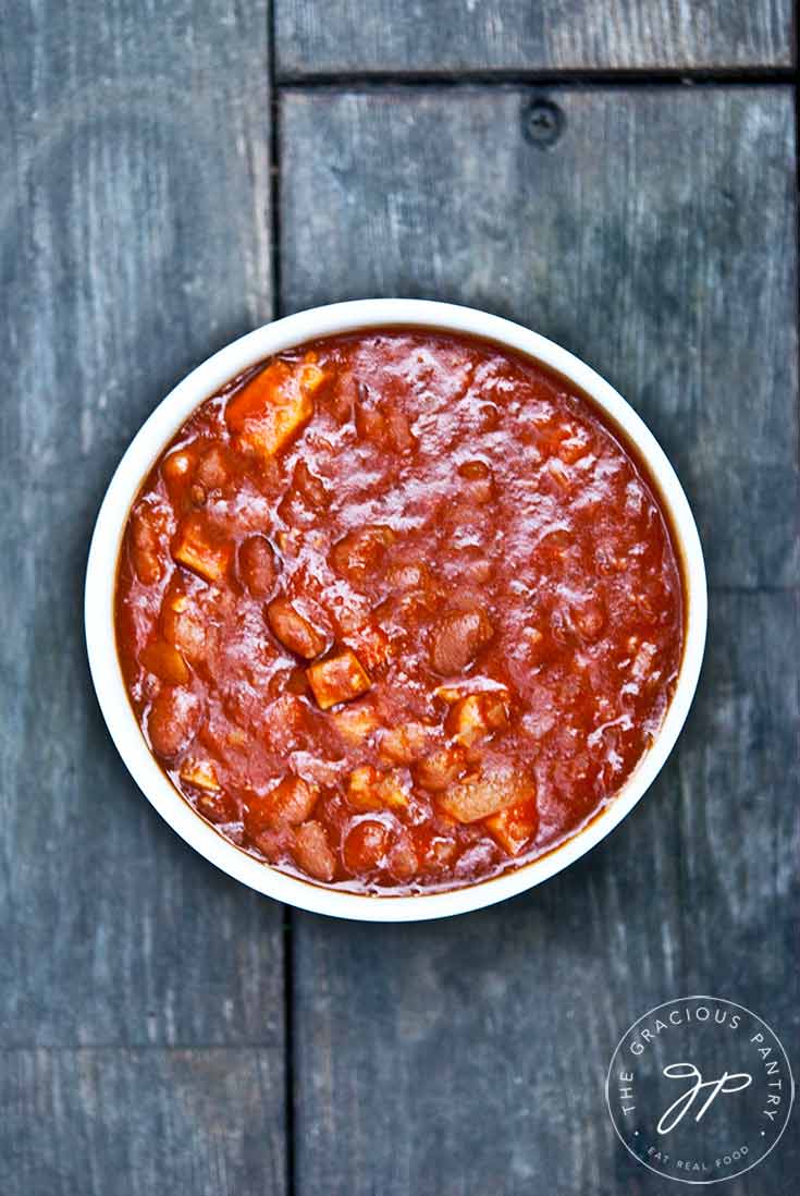 And overhead view of a white bowl on a wooden table filled with this delicious Pork And Beans Recipe.