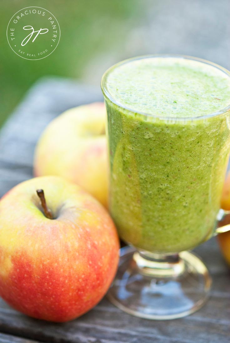 A Cinnamon Apple Smoothie is presented in a clear mug, surrounded by apples.