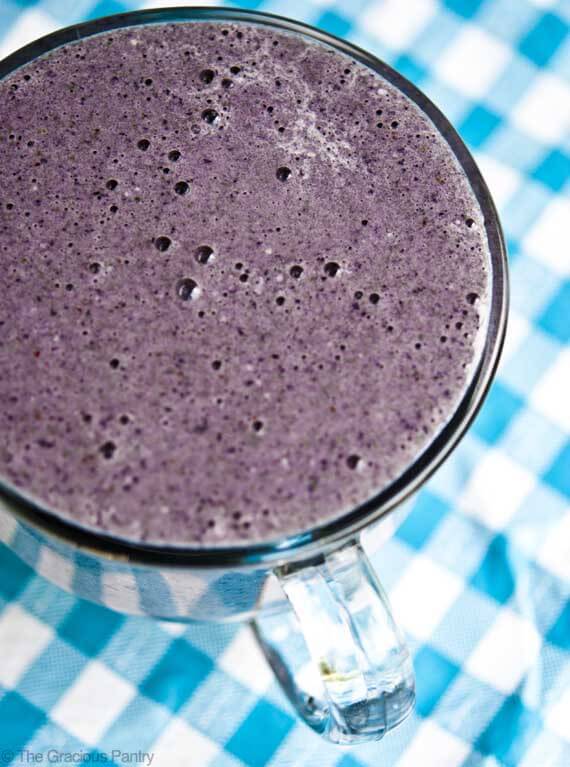 A close up shot of this Clean Eating Blueberry Banana Smoothie shows a vibrant, blueberry blue in a clear glass mug.
