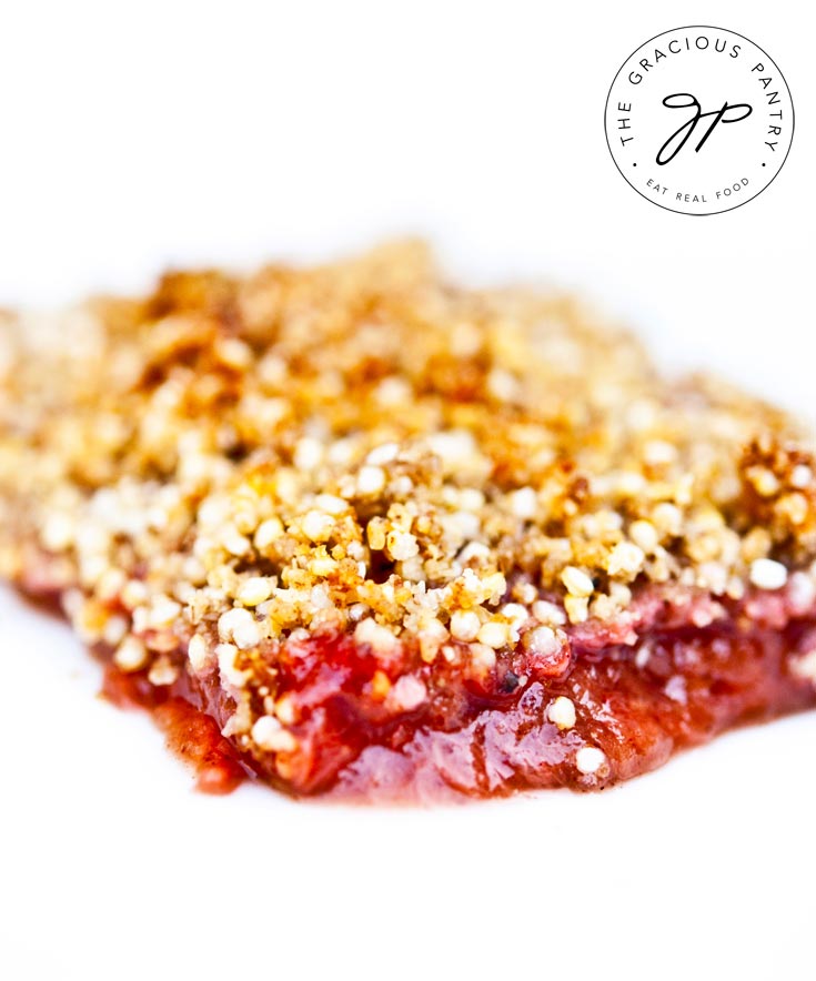 A slice of this Clean Eating Strawberry Rhubarb Apple Crisp sits on a completely white background. The crisp on top is a beautiful golden color while the rhubarb layer below is a beautiful, bright pink.