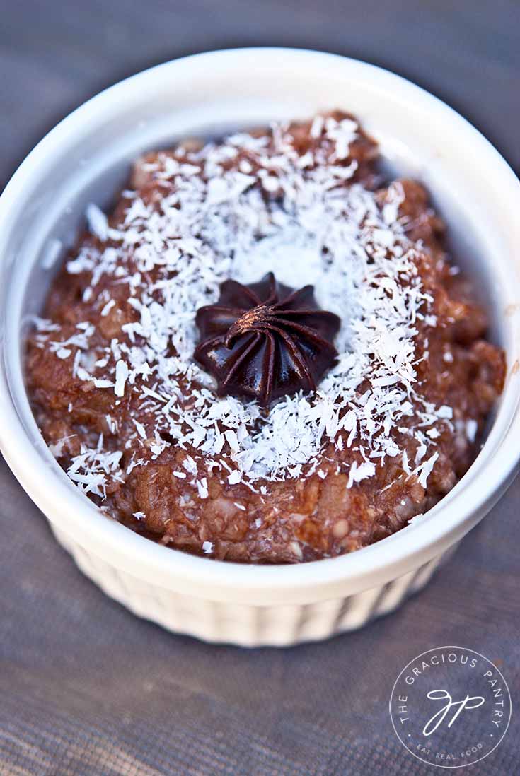 A white bowl sits on a wooden table filled with this German Chocolate Oatmeal Recipe.