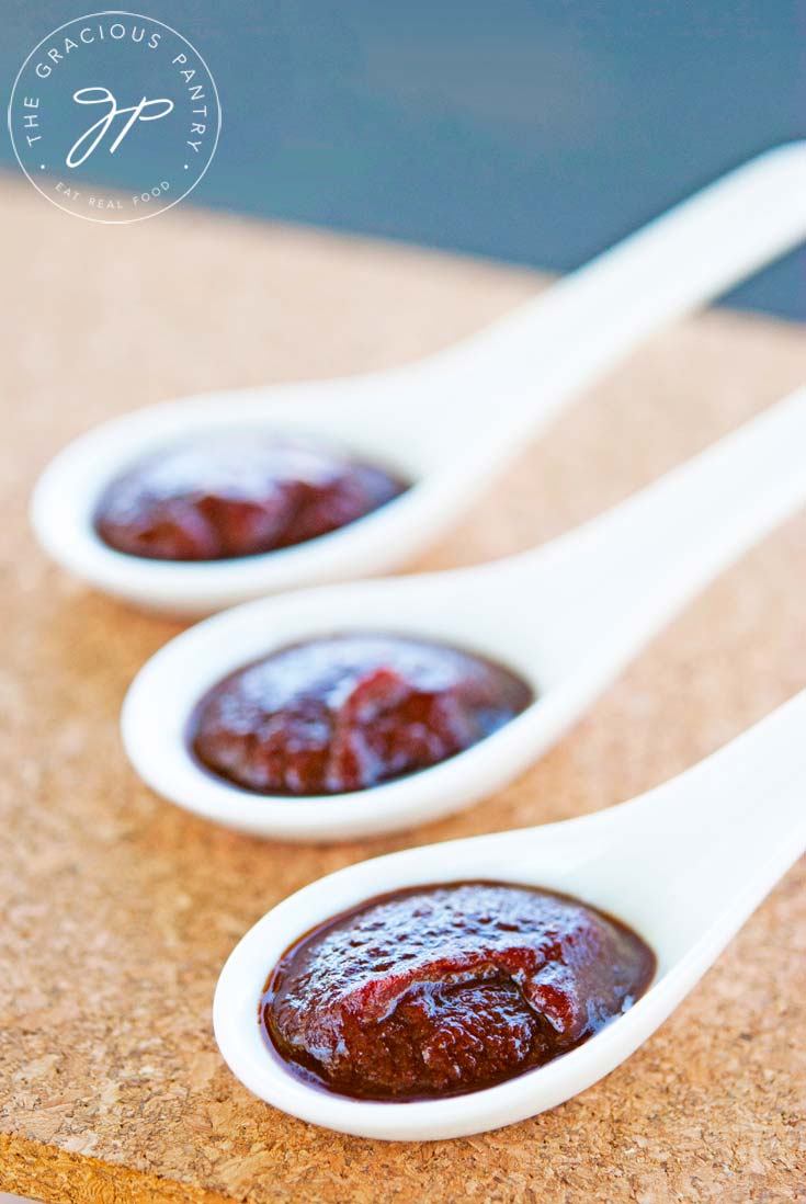 Clean Eating Barbecue Sauce shown in three white spoons lined up on a table. The sauce is a rich, reddish-brown color.