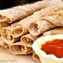 Chicken Taquitos piled up on a wood surface.