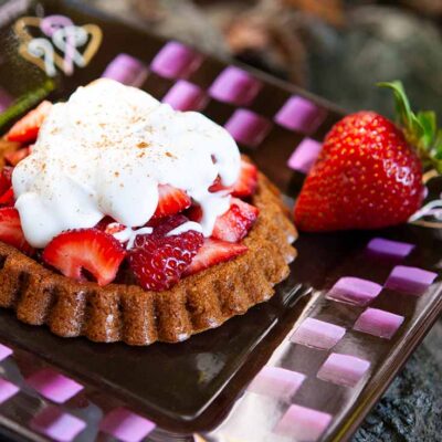 A plate holds a delicious looking strawberry shortcake. It has a golden brown base, a large pile of fresh, sweet strawberries and a dollop of whopped cream, all topped off with a sprinkle of cinnamon.