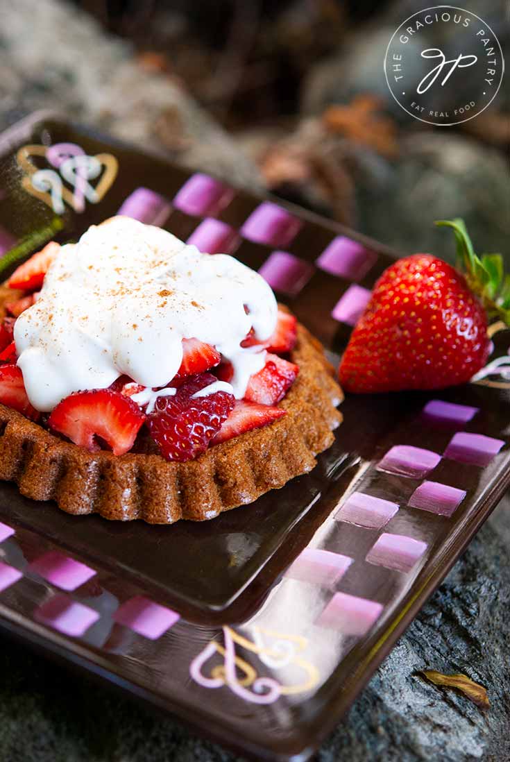 A plate holds a delicious looking strawberry shortcake. It has a golden brown base, a large pile of fresh, sweet strawberries and a dollop of whopped cream, all topped off with a sprinkle of cinnamon.