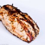 A grilled tarragon chicken breast sits on a white plate, ready to eat.