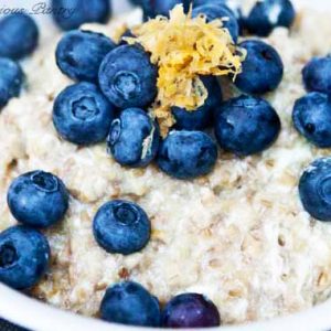 A close up of a bowl of lemon blueberry oatmeal in a white bowl with fresh blueberries and lemon zest on top.