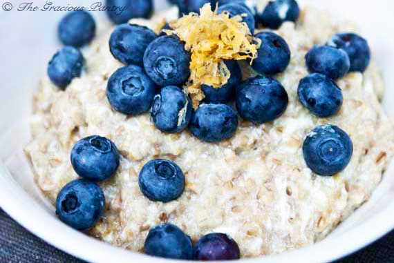 A close up of a bowl of lemon blueberry oatmeal in a white bowl with fresh blueberries and lemon zest on top.