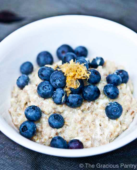 A white bowl filled with lemon blueberry oatmeal and topped with fresh blueberries and lemon zest.