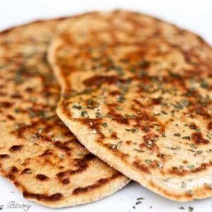 Two whole wheat naan on a white surface.