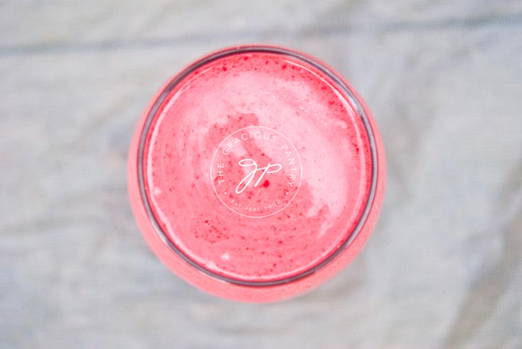 Clean Eating Raspberry Coconut Smoothie shown in a clear glass from overhead, looking down into the bright pink smoothie.