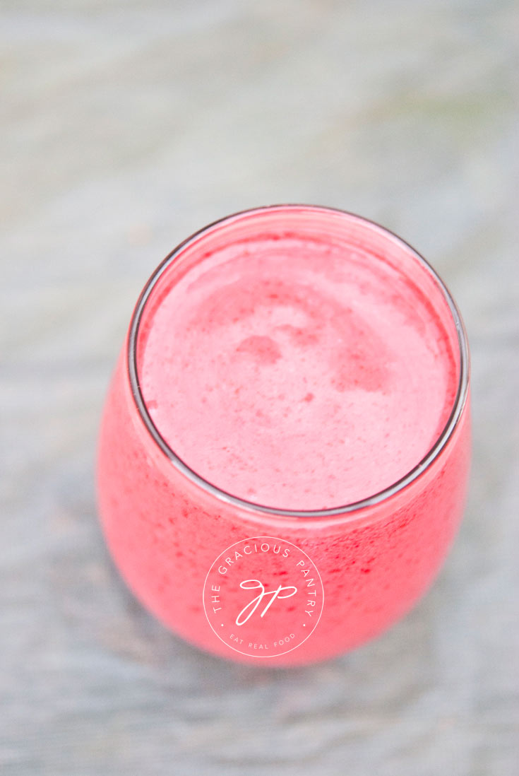 Clean Eating Raspberry Coconut Smoothie in a clear glass cup shown from the side. The smoothie is a very bright, raspberry pink color.