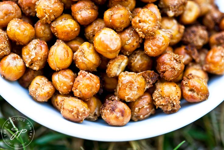 Clean Eating Roasted Chickpeas Recipe shown from overhead. Golden brown chickpeas are piled up in a white bowl, which is sitting on a green, grassy background.
