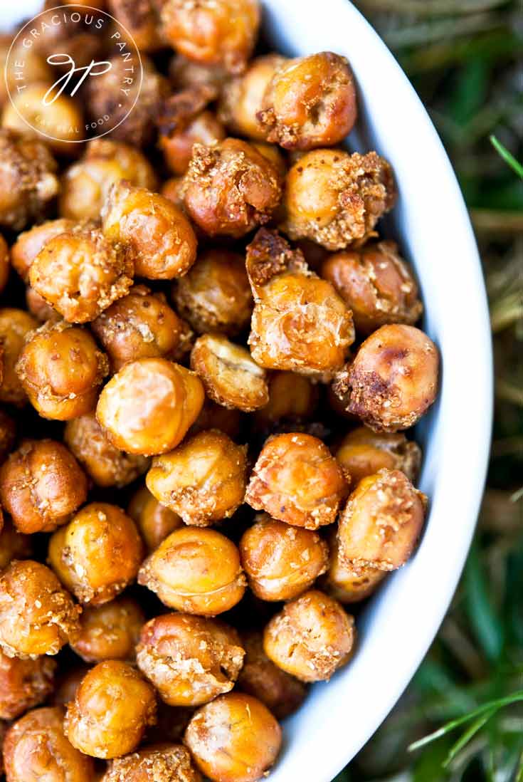 Clean Eating Roasted Chickpeas served in a white bowl and sitting on a green grassy background. Chickpeas are roasted to a rich, golden brown.